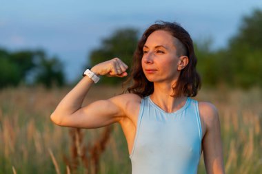 Mavi elbiseli ve beyaz şortlu bir kadın gün batımında tarlada poz veriyor. Spor figürü..