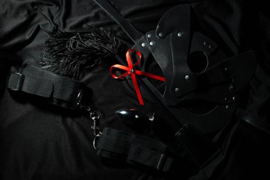 Sexy set of whip, cat mask, handcuffs and butt plug on black background