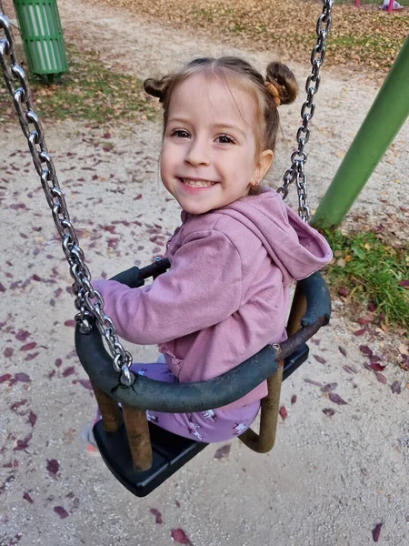 Happy little girl on a swing in the park. Child on playground. Swing Kid play outdoor
