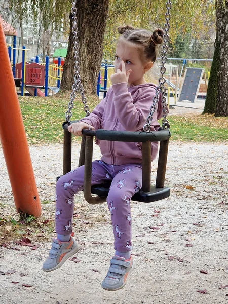 Happy little girl on a swing in the park. Child on playground. Swing Kid play outdoor