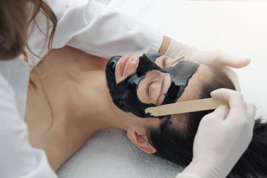 Kozmetik uzmanı güzel bir kadının yüzüne siyah maske takıyor. Kaplıcadaki muhteşem kadın yüz bakımı yaptırıyor.