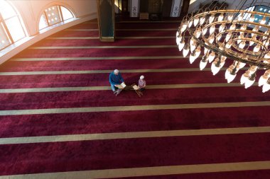 Müslüman adam oğluna Allah 'a dua etmeyi öğretiyor ve ona camide Kur' an okumayı öğretiyor..