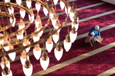 Müslüman adam oğluna Allah 'a dua etmeyi öğretiyor ve ona camide Kur' an okumayı öğretiyor..