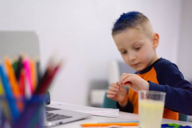 Ev ödevi yapan, defter ve modern aletler kullanan sevimli bir çocuk. Evde eğitim kavramı.