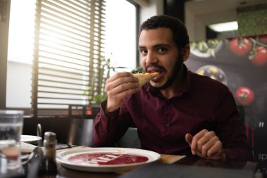 Pizza zamanı konsepti. Pozitif erkek Afrikalı ofis çalışanı ya da takım elbiseli girişimci büyük bir dilim pizza yiyor.