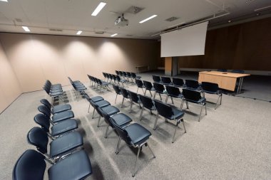 Modern konferans salonunda büyük bir sunum ekranı. Büyük bir sunum odası, sıralı sandalyeler ve bir podyum, kurumsal bir etkinliğe hazır.
