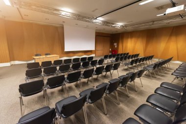 Modern konferans salonunda büyük bir sunum ekranı. Büyük bir sunum odası, sıralı sandalyeler ve bir podyum, kurumsal bir etkinliğe hazır.