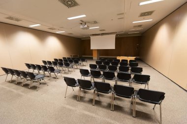 Modern konferans salonunda büyük bir sunum ekranı. Büyük bir sunum odası, sıralı sandalyeler ve bir podyum, kurumsal bir etkinliğe hazır.