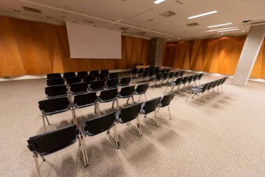 Modern konferans salonunda büyük bir sunum ekranı. Büyük bir sunum odası, sıralı sandalyeler ve bir podyum, kurumsal bir etkinliğe hazır.