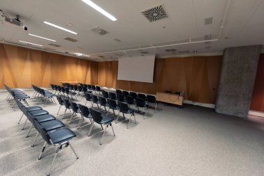 Modern konferans salonunda büyük bir sunum ekranı. Büyük bir sunum odası, sıralı sandalyeler ve bir podyum, kurumsal bir etkinliğe hazır.