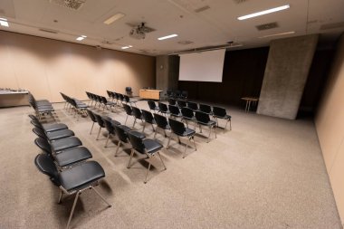 Modern konferans salonunda büyük bir sunum ekranı. Büyük bir sunum odası, sıralı sandalyeler ve bir podyum, kurumsal bir etkinliğe hazır.