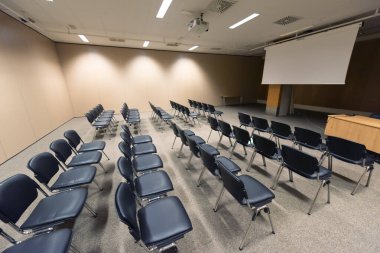 Modern konferans salonunda büyük bir sunum ekranı. Büyük bir sunum odası, sıralı sandalyeler ve bir podyum, kurumsal bir etkinliğe hazır.