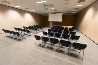 Modern konferans salonunda büyük bir sunum ekranı. Büyük bir sunum odası, sıralı sandalyeler ve bir podyum, kurumsal bir etkinliğe hazır.