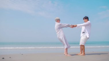 Asyalı emekli çift yazın deniz kenarında dinleniyor. Sahilde partneriyle dans eden son sınıf öğrencisi bir kadın..