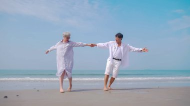 Asyalı emekli çift yazın deniz kenarında dinleniyor. Sahilde partneriyle dans eden son sınıf öğrencisi bir kadın..