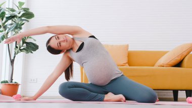 Spor giyimli güzel Asyalı hamile kadın evde yoga yapıyor..