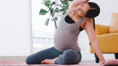 Spor giyimli güzel Asyalı hamile kadın evde yoga yapıyor..