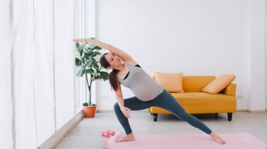 Spor giyimli güzel Asyalı hamile kadın evde yoga yapıyor..