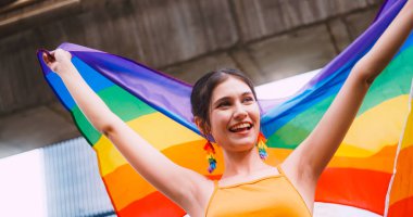 Genç bir kadın gurur yürüyüşü sırasında homoseksüelliğin sembolü olan gökkuşağı bayrağını sallıyor..