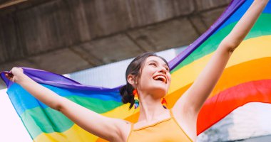 Genç bir kadın gurur yürüyüşü sırasında homoseksüelliğin sembolü olan gökkuşağı bayrağını sallıyor..