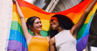 Lezbiyen bir çift, gurur yürüyüşü sırasında homoseksüelliğin sembolü olan gökkuşağı bayrağını sallıyor..
