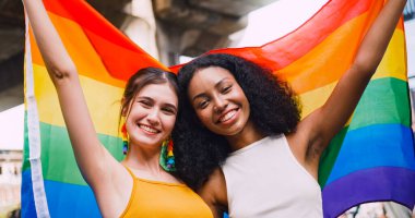 Lezbiyen bir çift, gurur yürüyüşü sırasında homoseksüelliğin sembolü olan gökkuşağı bayrağını sallıyor..