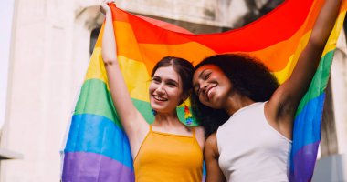 Lezbiyen bir çift, gurur yürüyüşü sırasında homoseksüelliğin sembolü olan gökkuşağı bayrağını sallıyor..