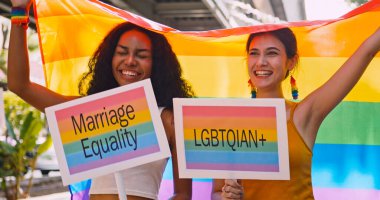 Lezbiyen bir çift, gurur yürüyüşü sırasında homoseksüelliğin sembolü olan gökkuşağı bayrağını sallıyor..
