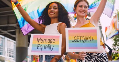 Lezbiyen bir çift, gurur yürüyüşü sırasında homoseksüelliğin sembolü olan gökkuşağı bayrağını sallıyor..