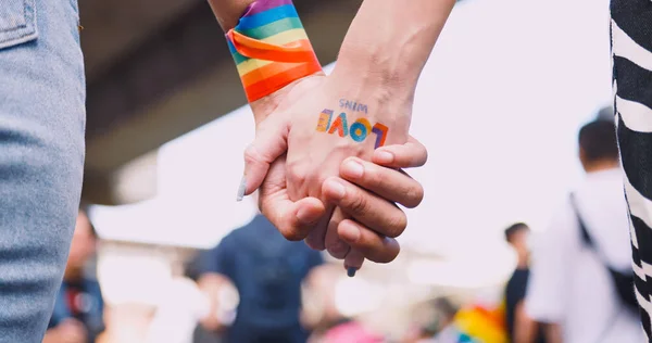 A couple\'s hands with a rainbow tattoo sticker representing the symbol of homosexuality in a pride parade.