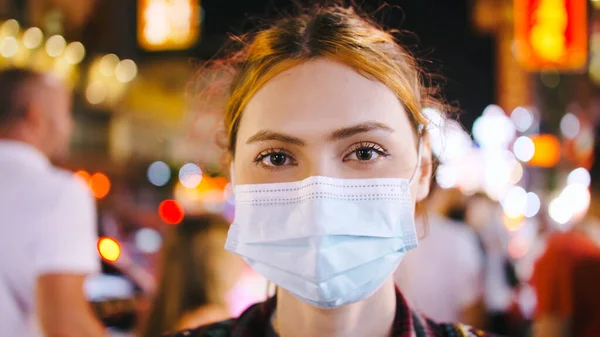 夜の街路に立っている間 医療マスクを着ている観光客の女性の肖像画 ストック画像