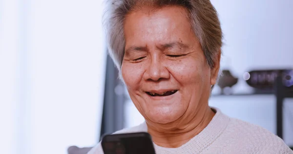 Mutlu Asyalı Yaşlı Kadın Evde Kanepede Otururken Akıllı Telefon Kullanıyor — Stok fotoğraf