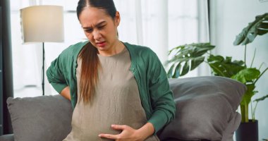 Asyalı hamile kadın evdeki kanepede dinlenirken sırt ağrısı çekiyor..