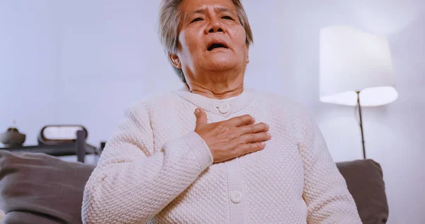 Asian old woman having difficulty breathing while sitting on the sofa at home.