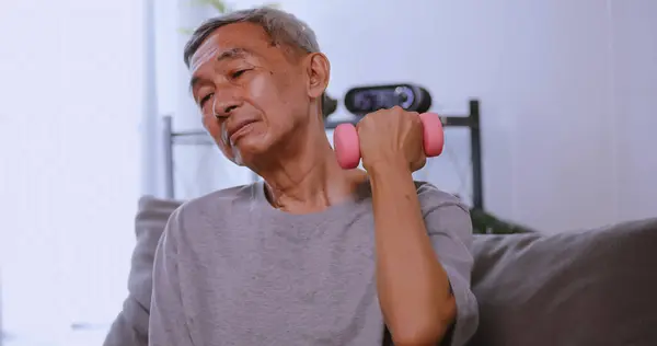 Asian old man doing exercise with dumbbells at home. Elderly man maintains her health by working out in every day.