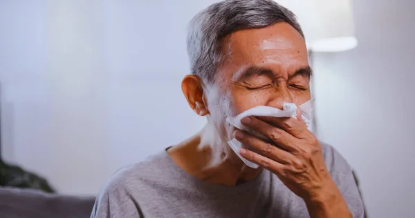 Asian elderly man suffering from allergies sneezing.