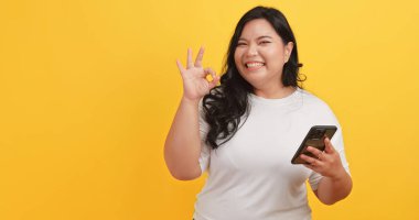 Beyaz tişört giyen tombul bir Asyalı kadın telefonunda sarı arka planda bir mesaj görünce heyecanlandı ve mutlu oldu.