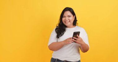 Beyaz tişört giyen tombul bir Asyalı kadın telefonunda sarı arka planda bir mesaj görünce heyecanlandı ve mutlu oldu.