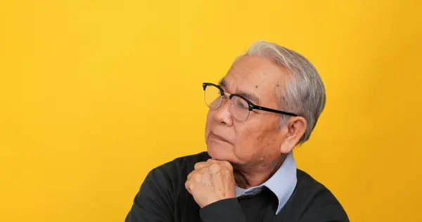 An old Asian man is thinking and deciding something. Isolated on yellow background in the studio.