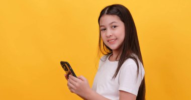 Sarı arka planda akıllı telefon kullanan sevimli küçük kız..