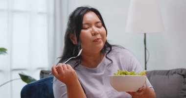 Tombul bir Asyalı kadın evdeki kanepede dinlenirken salata yemekten hoşlanır..