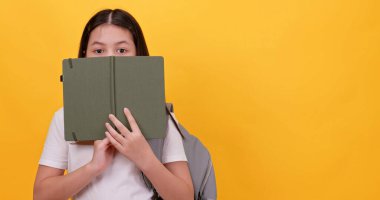 Sevimli liseli kız okul çantası taşıyor ve sarı arka planda bir defter tutuyor..