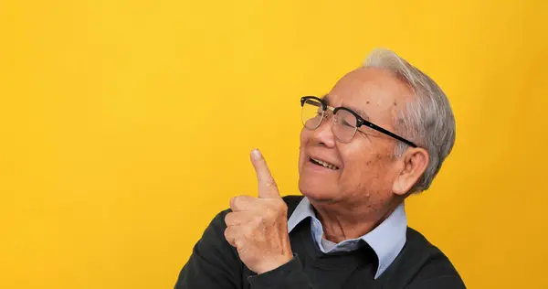 An old Asian man is thinking and deciding something. Isolated on yellow background in the studio.