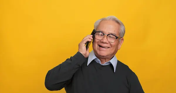 Asian old man using smart phone. Isolated on yellow background in the studio.