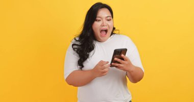 Beyaz tişört giyen tombul bir Asyalı kadın telefonunda sarı arka planda bir mesaj görünce heyecanlandı ve mutlu oldu.