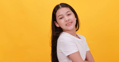 Beyaz tişörtlü, sarı arka planda duran tatlı küçük bir kız..