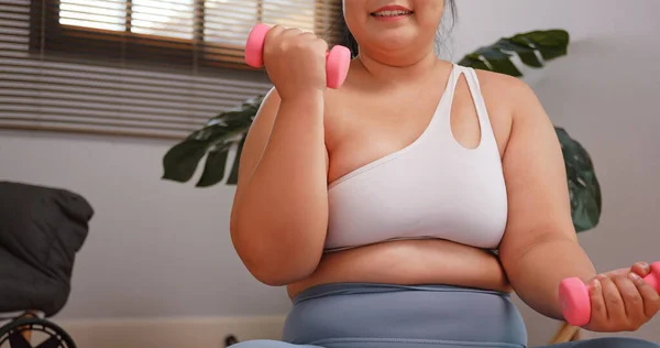 A chubby Asian woman in sportswear exercising to lose weight at home. Fat woman exercising by lifting dumbbells.