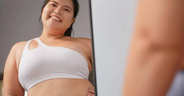 A chubby Asian woman feels confident and proud of her body while standing in front of the mirror.