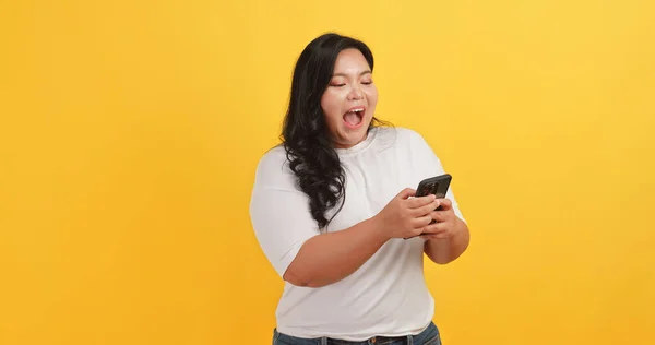 A chubby Asian woman wearing a white t-shirt was excited and happy when she saw a message on her phone on a yellow background