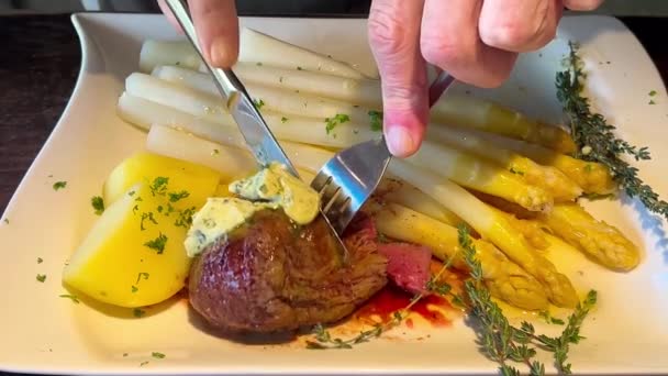 手与刀叉切蒸中等罕见的牛排盘与白色芦笋芽和新土豆 德国菜中流行的一道菜 芦笋季节 高质量的4K镜头 — 图库视频影像